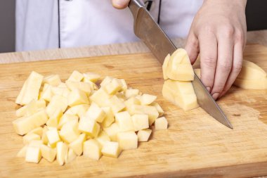 Aşçı patatesleri ahşap bir tahtada keser, yemek hazırlar.