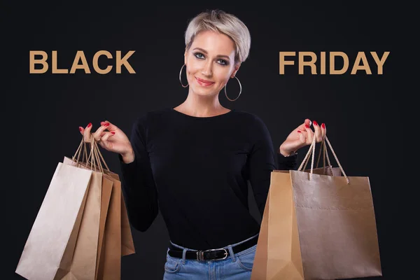 Mujer de compras sosteniendo bolsas de artesanía aisladas sobre fondo negro con copyspace en vacaciones de viernes negro. Viernes negro concepto de venta . — Foto de Stock