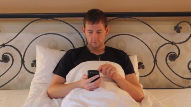 若い男のベッドで携帯電話で仕事 — ストック動画