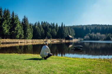 Young man sit on nice clean pond with wooden building and spring