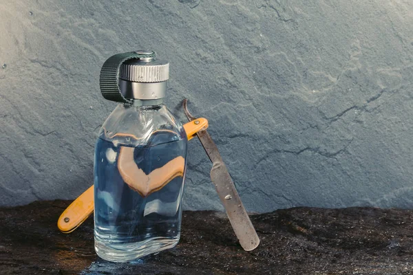 Limpar garrafa aftershave azul com navalha velha na textura de pedra molhada — Fotografia de Stock