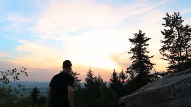 Genç adam gün batımı sırasında kaya üzerinde el