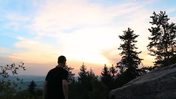 若い男は日没時に岩の上に手を差し伸べた — ストック動画