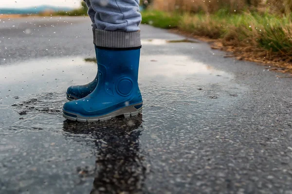 Young boy jump into puddle with gumboots and splash water on str — Stock Photo, Image