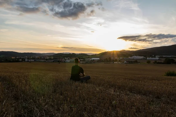 Gün batımında biçilmiş alanda oturan genç adam, Çek Cumhuriyeti — Stok fotoğraf