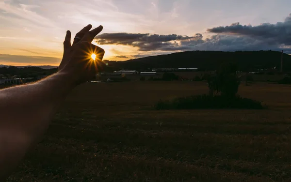 Man hand catch sun at sunset on field with dramatic sky. Czech l