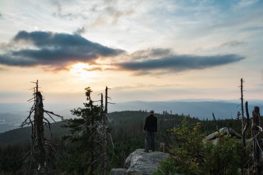 Lan gün batımında kaya üzerinde duran beyaz şapkalı genç bir turist