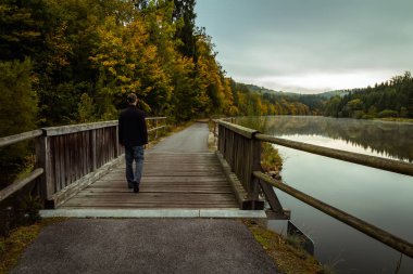 Vltava nehri ve sonbahar ile tahta köprüde yürüyen genç adam 