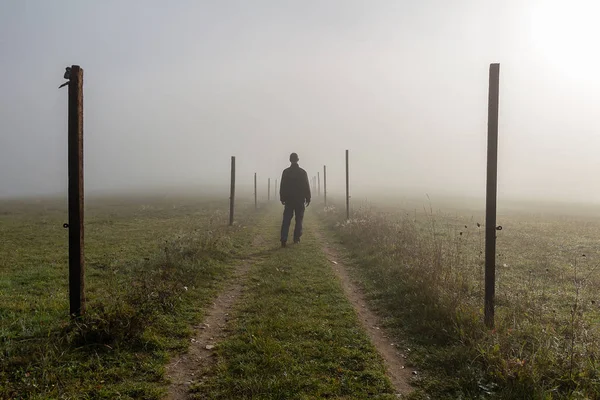 Young man walk on path with wooden stick in misty fog at sunrise — Stock Photo, Image