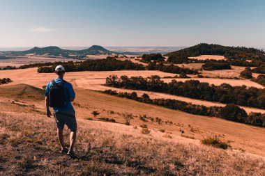 Sırt çantalı genç adam tepeden iniyor ve gün doğumunda Çek merkez dağ vadisine bakıyor.
