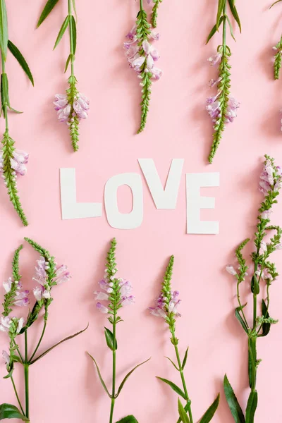 Word Love made of letters cut out of paper. Pattern made of wild flowers on a pink pastel background