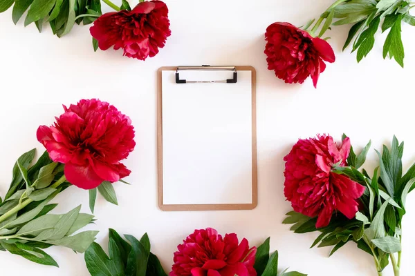 Clipboard with blank paper. Wreath made of red peonies