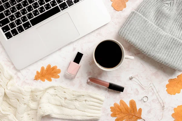 Beige textured desk with laptop, mug of coffee, dry leaves,  women's clothes, accessories and cosmetics