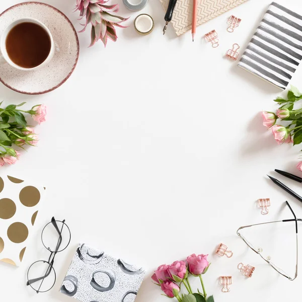 Round frame made of mug of coffee, flowers, glasses and stationery on white background