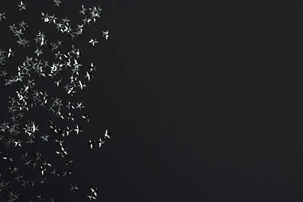 Silver stars confetti on a black background. Festive backdrop with copy space.