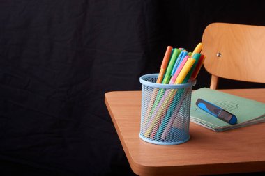 Siyah arka plan üzerine okulda masa mavi metal sepetteki renkli kalemler