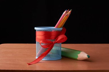 Siyah ahşap masa üzerinde büyük yeşil kalem ile teneke kutuda renkli kalemler