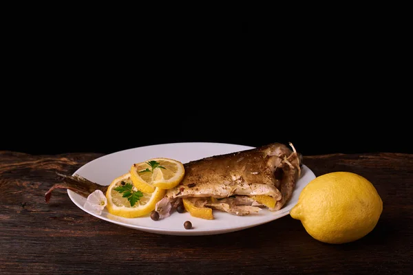 Appetizing baked fish, covered with juicy lemons, garlic and salt on side, above view