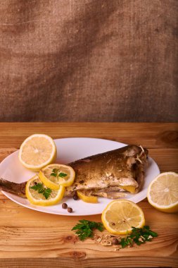 Limon, baharatlar ve otlar ahşap arka plan üzerinde beyaz tabakta Fırında Balık