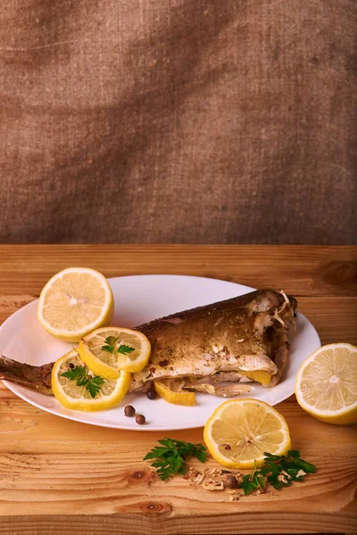 Limon, baharatlar ve otlar ahşap arka plan üzerinde beyaz tabakta Fırında Balık
