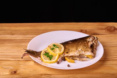 Limon, baharatlar ve otlar ahşap arka plan üzerinde beyaz tabakta Fırında Balık