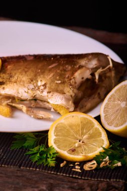 Limon, baharatlar ve otlar ahşap arka plan üzerinde beyaz tabakta Fırında Balık