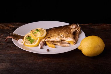 Limon, baharatlar ve otlar ahşap arka plan üzerinde beyaz tabakta Fırında Balık