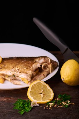 Düzenlenen lemonwith siyah bıçak ve plaka baharat ve otlar ile ızgara balık sos ile