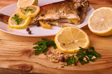 Limon, baharatlar ve otlar ahşap arka plan üzerinde beyaz tabakta Fırında Balık