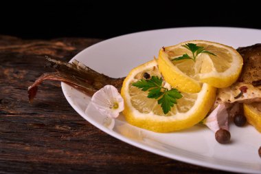 Limon, baharatlar ve otlar ahşap arka plan üzerinde beyaz tabakta Fırında Balık