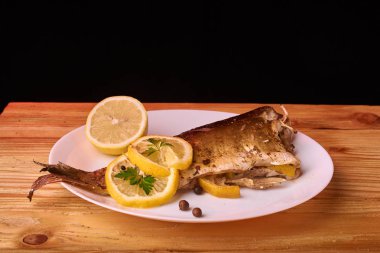 Limon, baharatlar ve otlar ahşap arka plan üzerinde beyaz tabakta Fırında Balık