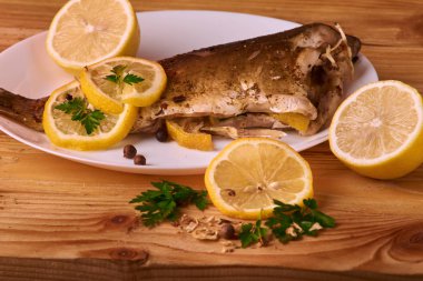 Limon, baharatlar ve otlar ahşap arka plan üzerinde beyaz tabakta Fırında Balık