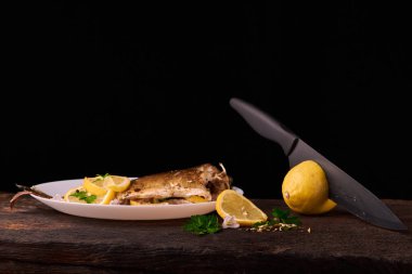 Düzenlenen lemonwith siyah bıçak ve plaka baharat ve otlar ile ızgara balık sos ile