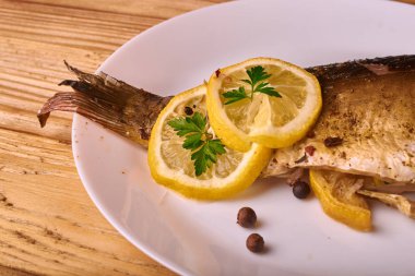Limon, baharatlar ve otlar ahşap arka plan üzerinde beyaz tabakta Fırında Balık