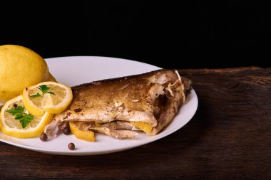 Limon, baharatlar ve otlar ahşap arka plan üzerinde beyaz tabakta Fırında Balık