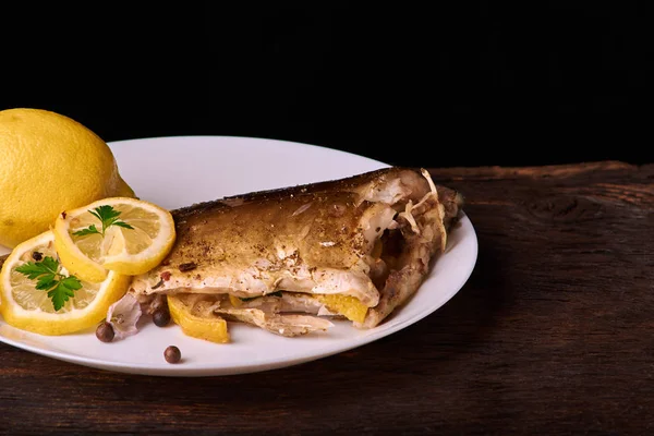 Limon, baharatlar ve otlar ahşap arka plan üzerinde beyaz tabakta Fırında Balık