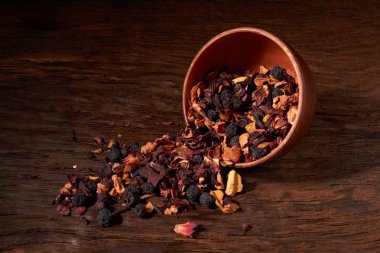 bir ahşap masa ve siyah arka plan üzerinde bir kil kase meyve çayı.