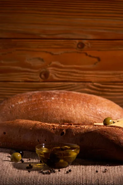 Свежий хлеб багет с оливковым маслом, оливки. сыр и розмарин на деревянном фоне. Вкусный завтрак — стоковое фото