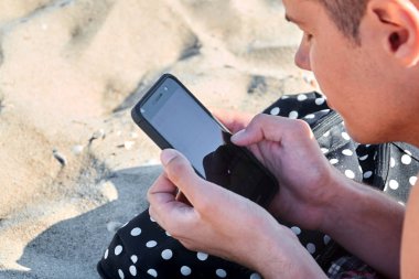 Sahilde bir cep telefonu tutan bir adamın elleri mockup görüntüsü. Seçici odak