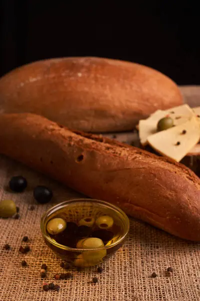 Fresh bread baguette with olive oil, olives. cheese and rosemary on wooden background. Teasty breakfast — Stock Photo, Image