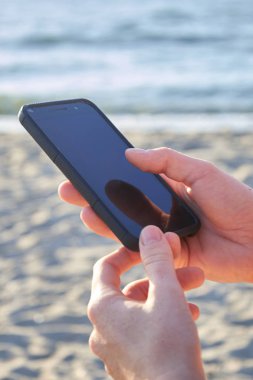 Sahilde bir cep telefonu tutan bir kadının elleri mockup görüntüsü. Seçici odak