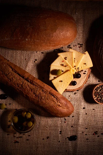 Traditional Dutch semi hard cheese served with olives on rural table with sacking. With baguette and bread — Stock Photo, Image