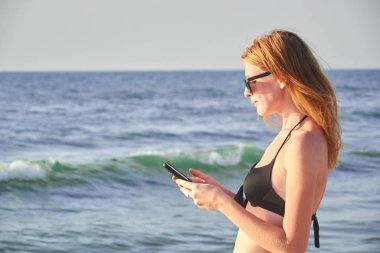 Sahilde bir cep telefonu tutan bir kadının elleri mockup görüntüsü. Seçici odak