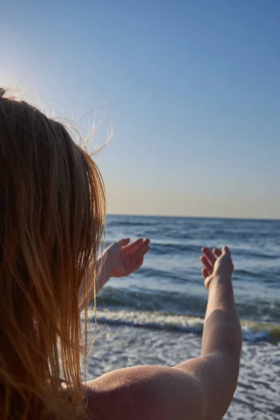 女人从后背看大海,赤身裸体,有风的头发。女孩把手伸向大海 — 图库照片