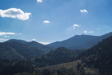 Bulutlar ve iğne yapraklı ormanlarla güneşli bir günde dağlar. Manzara