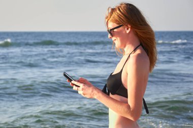 Sahilde bir cep telefonu tutan bir kadının elleri mockup görüntüsü. Seçici odak