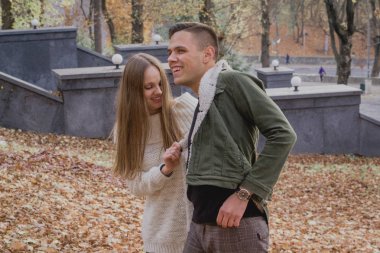 Sonbahar üzerinde aşk stand çift bir parkta yaprakları düşmüş, güzel bir sonbahar günü zevk. Adam hugs kız