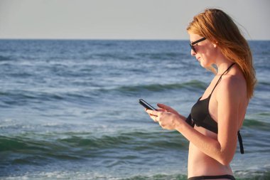 Sevimli gülümseyen kız manifatura bir plajda cep telefonu mesajı ile. Nice sakin ol