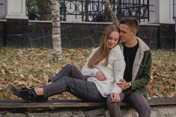 Couple in love stand on autumn fallen leaves in a park, enjoying a beautiful autumn day. Man hugs girl — Stock Photo, Image