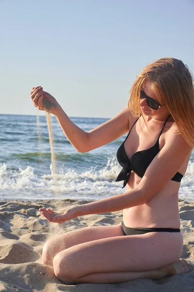 Piękna kobieta siedzi na plaży wpisując piasku w jej ręce na tle morza — Zdjęcie stockowe
